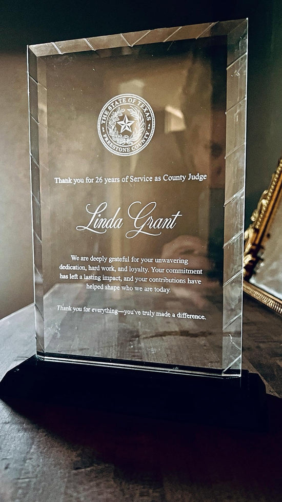 A clear glass engraved award plaque on a black base, engraved with a county judge retirement message 
